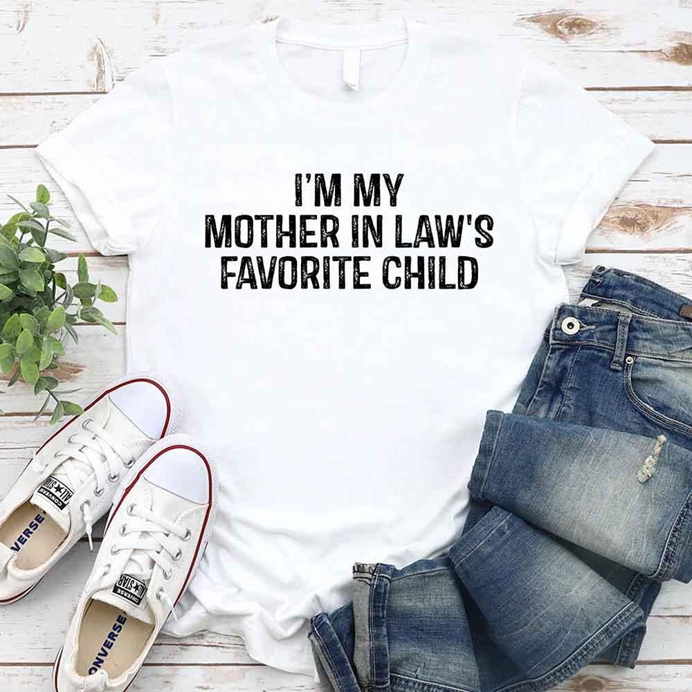 White crew-neck T-shirt with bold text “I’M MY MOTHER IN LAW’S FAVORITE CHILD”.