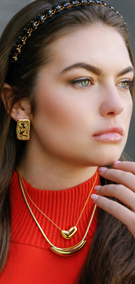 Gold square stud earrings with embossed face detail, worn on model’s ear