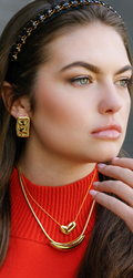 Gold square stud earrings with embossed face detail, worn on model’s ear