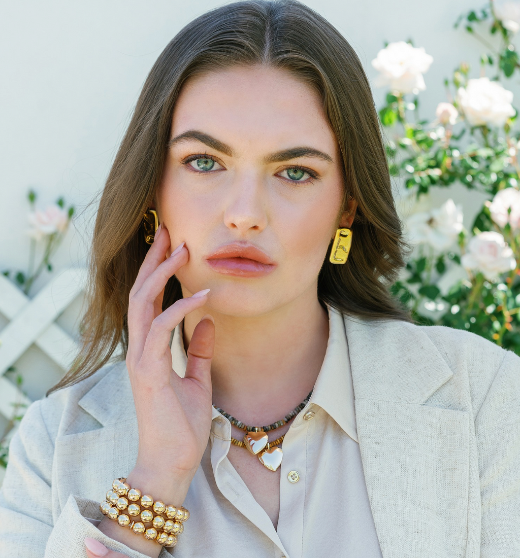 Gold square stud earrings with embossed face detail, worn with necklace and bracelet