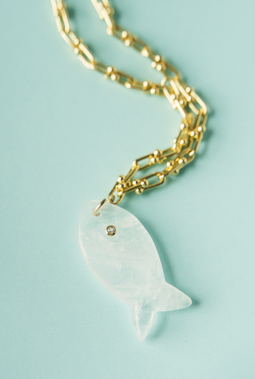 Gold fish pendant necklace detail with white fish charm and small round stud.