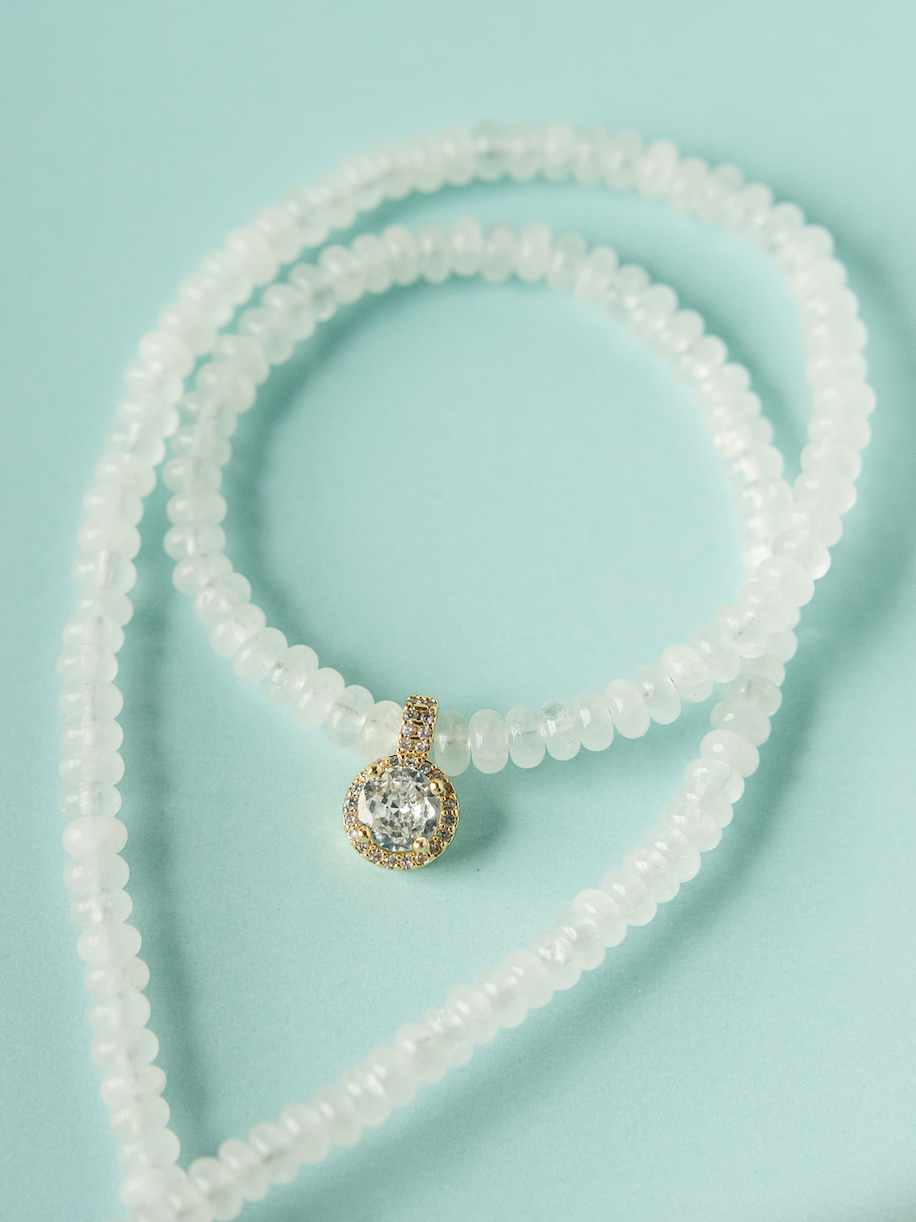 White beaded necklace with round gold-toned pendant and sparkling center