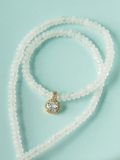 White beaded necklace with round gold-toned pendant and sparkling center