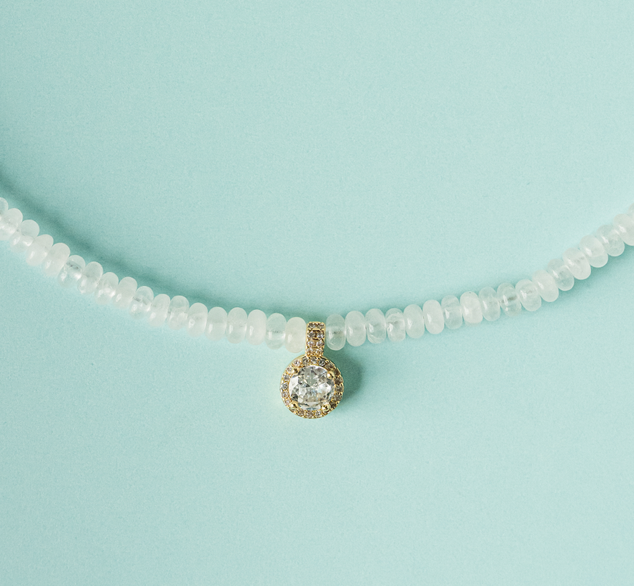 White beaded necklace close-up: round gold-toned charm with sparkling center