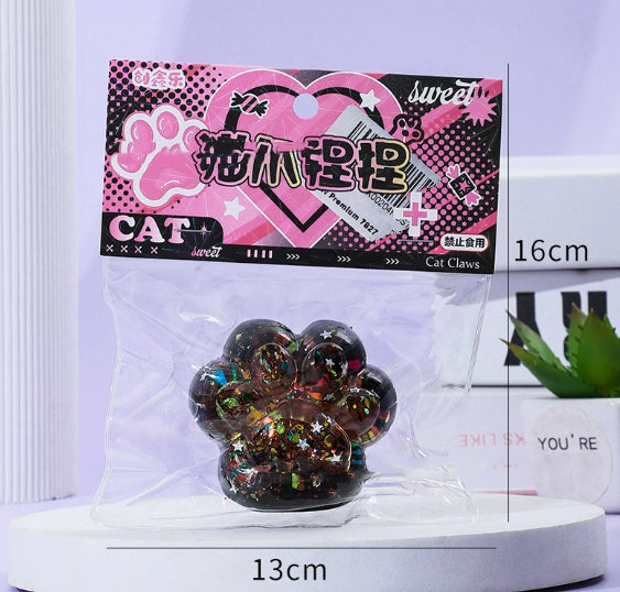 Dark glitter cat paw stress toy with green and gold tones in blister pack