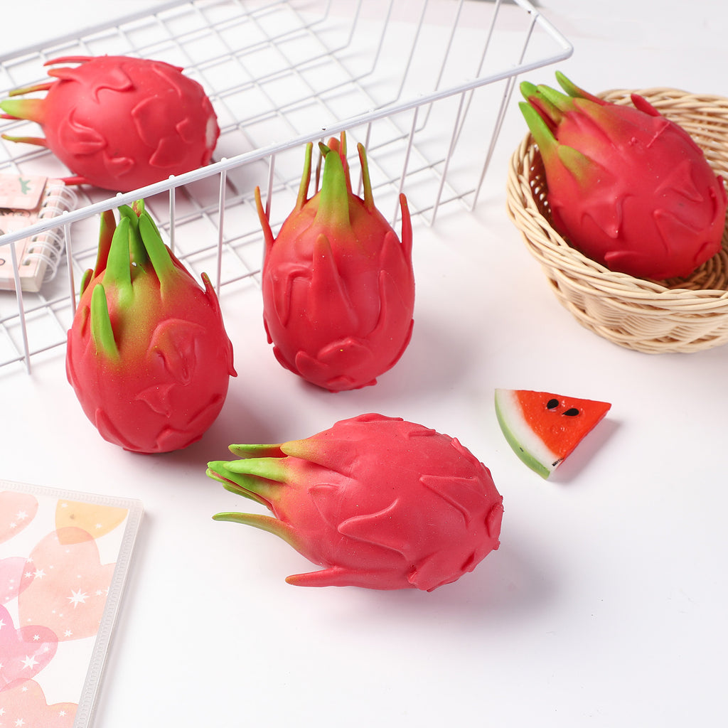 Red dragon fruit stress-relief gag toy cluster with green leafy tops, on tabletop