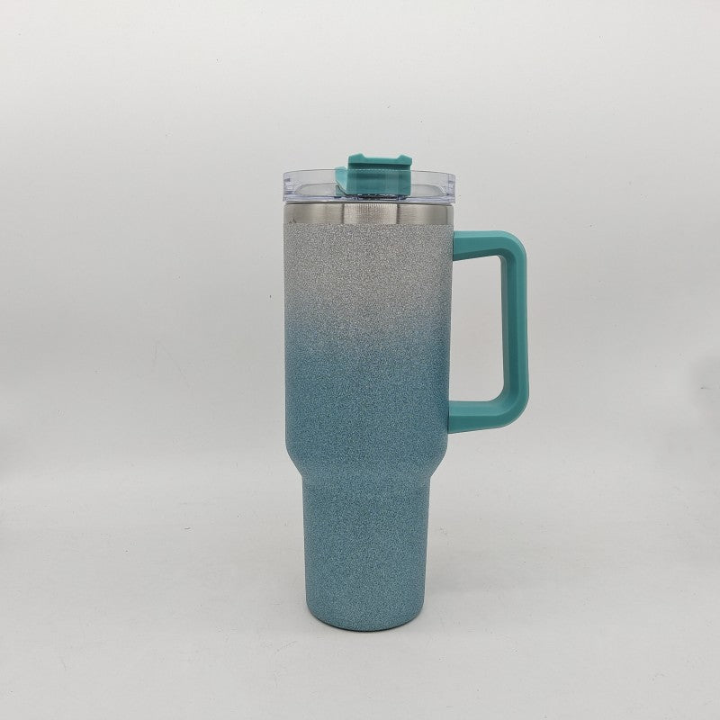 Insulated stainless steel tumbler with gray-to-teal gradient finish, handle, and clear lid