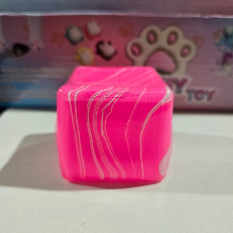 Pink cube squeeze stress-relief toy with white wavy lines on top and sides.