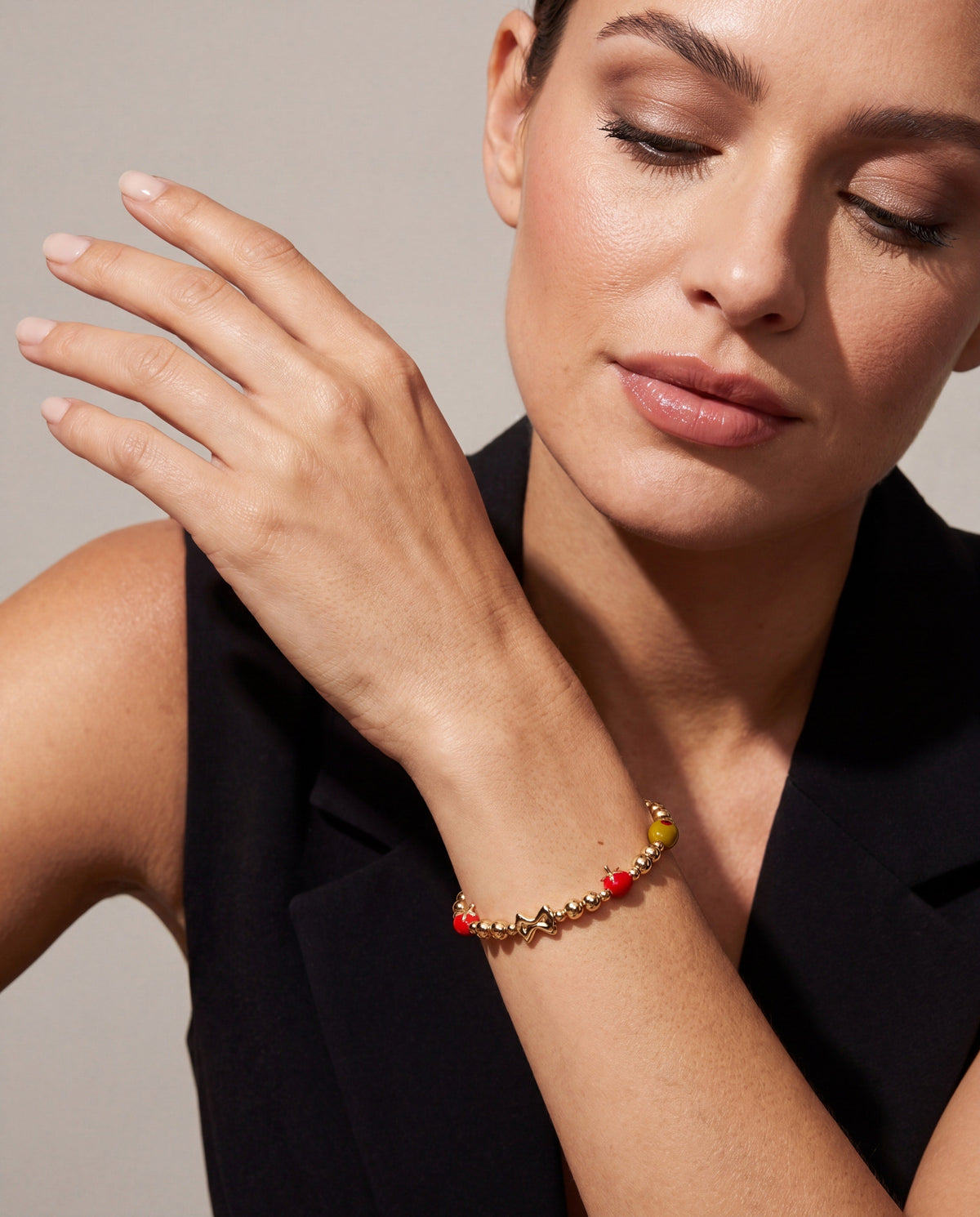 Gold-tone beaded bangle bracelet with red accents on model's wrist
