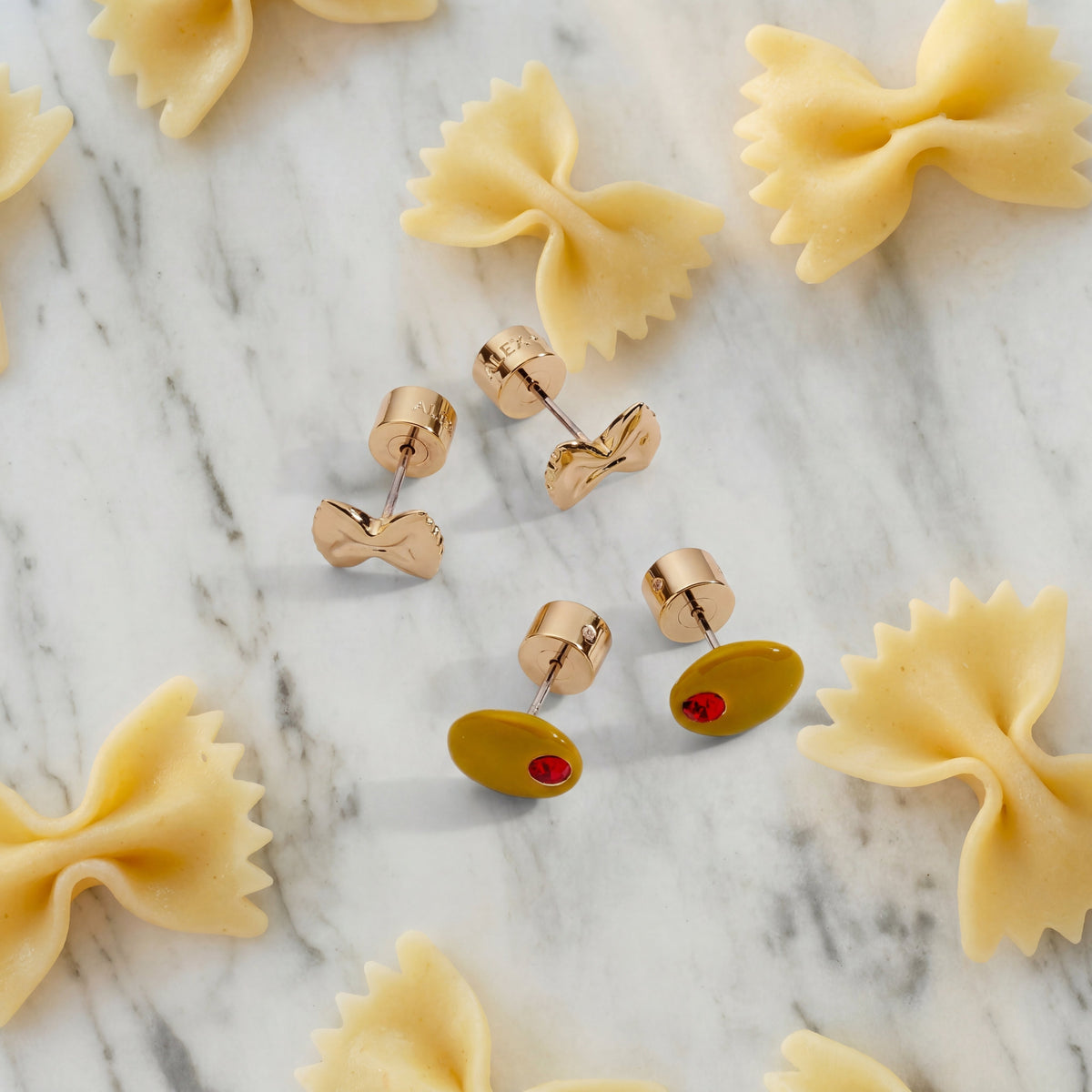 Gold pasta bow and oval stud earrings with red gemstones on marble, set of 2