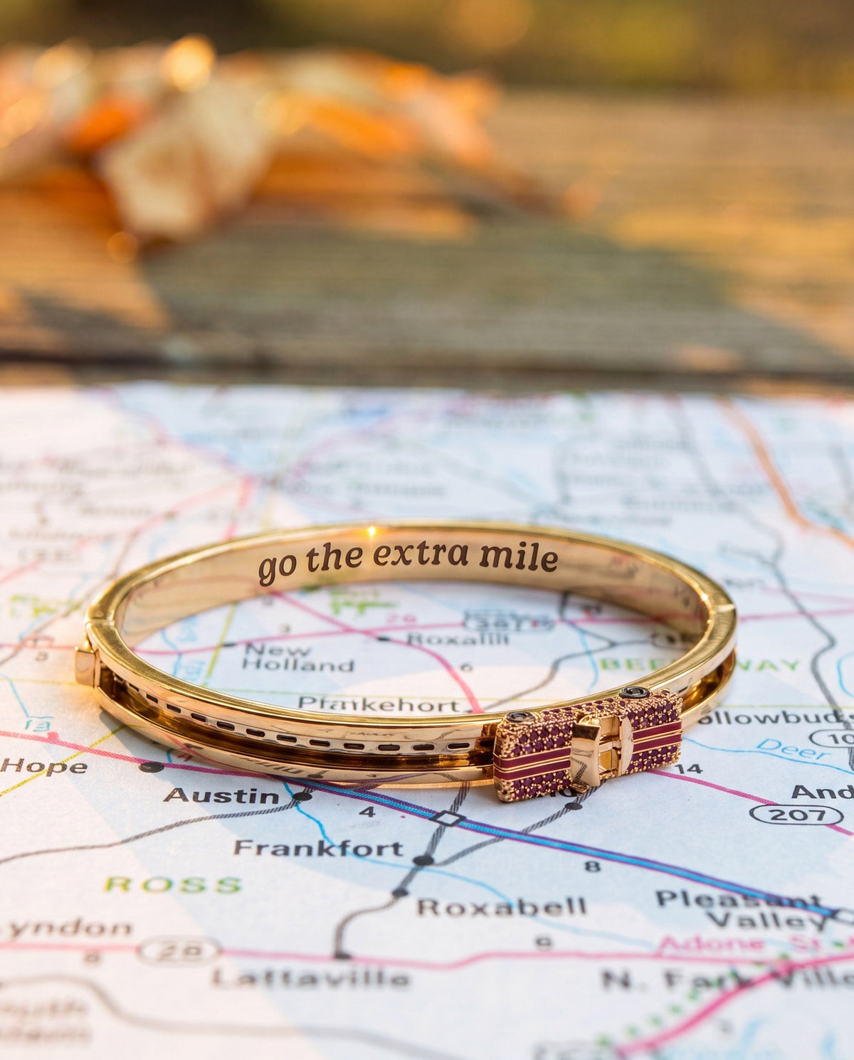 Gold-tone car fidget bangle with pink crystal clasp and “go the extra mile” text