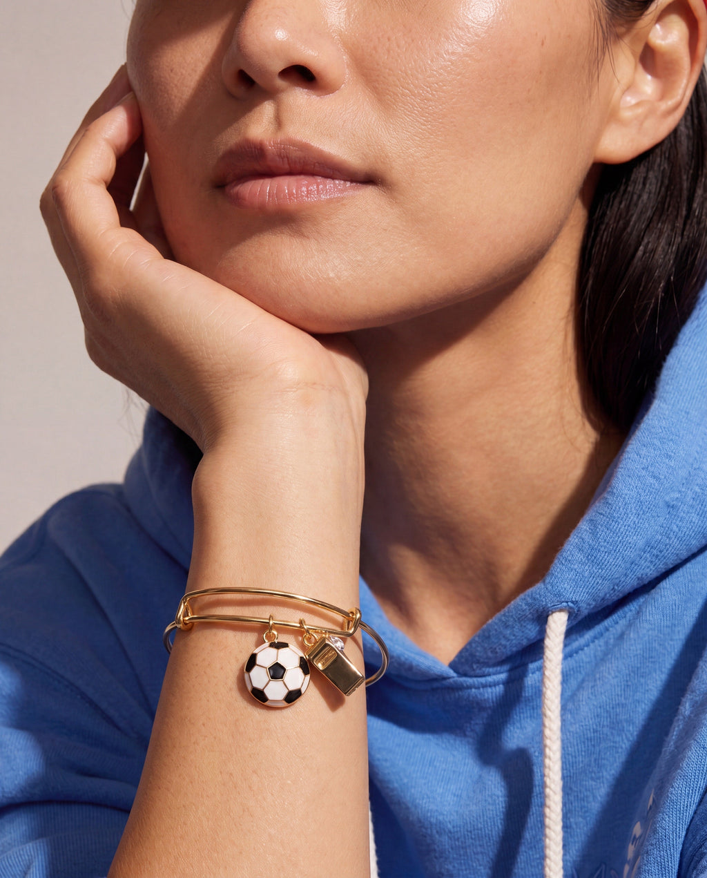 Gold bangle on wrist with soccer-ball and whistle charms