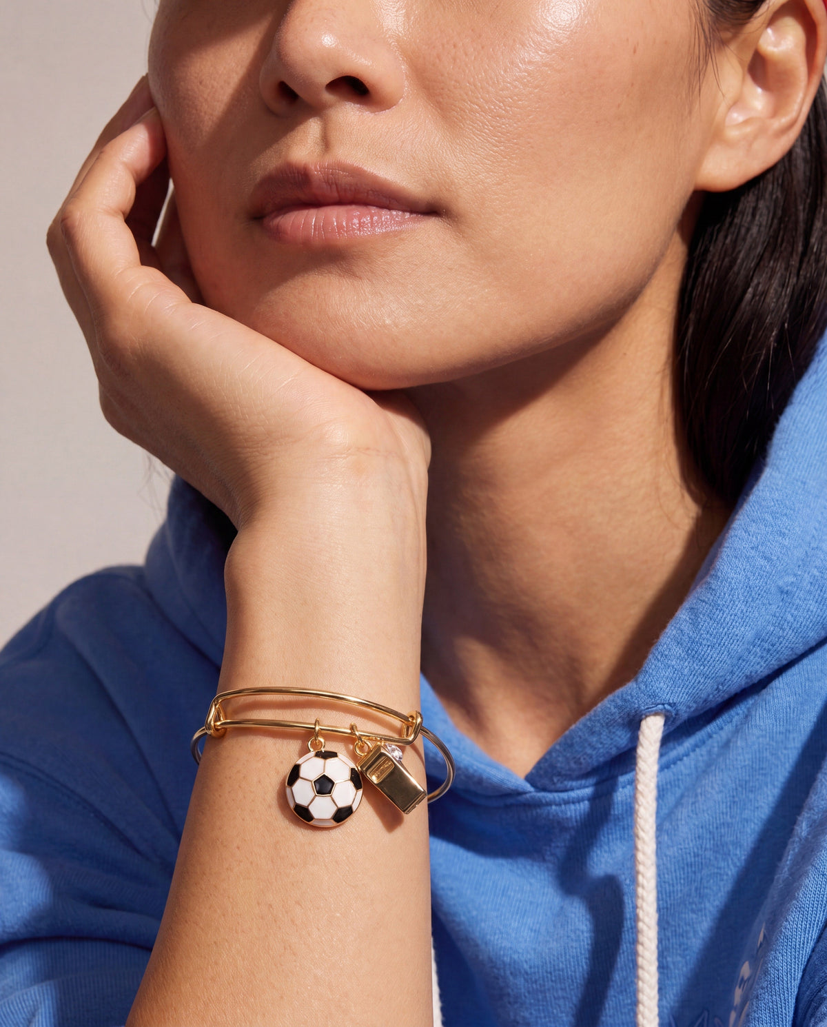 Gold bangle on wrist with soccer-ball and whistle charms