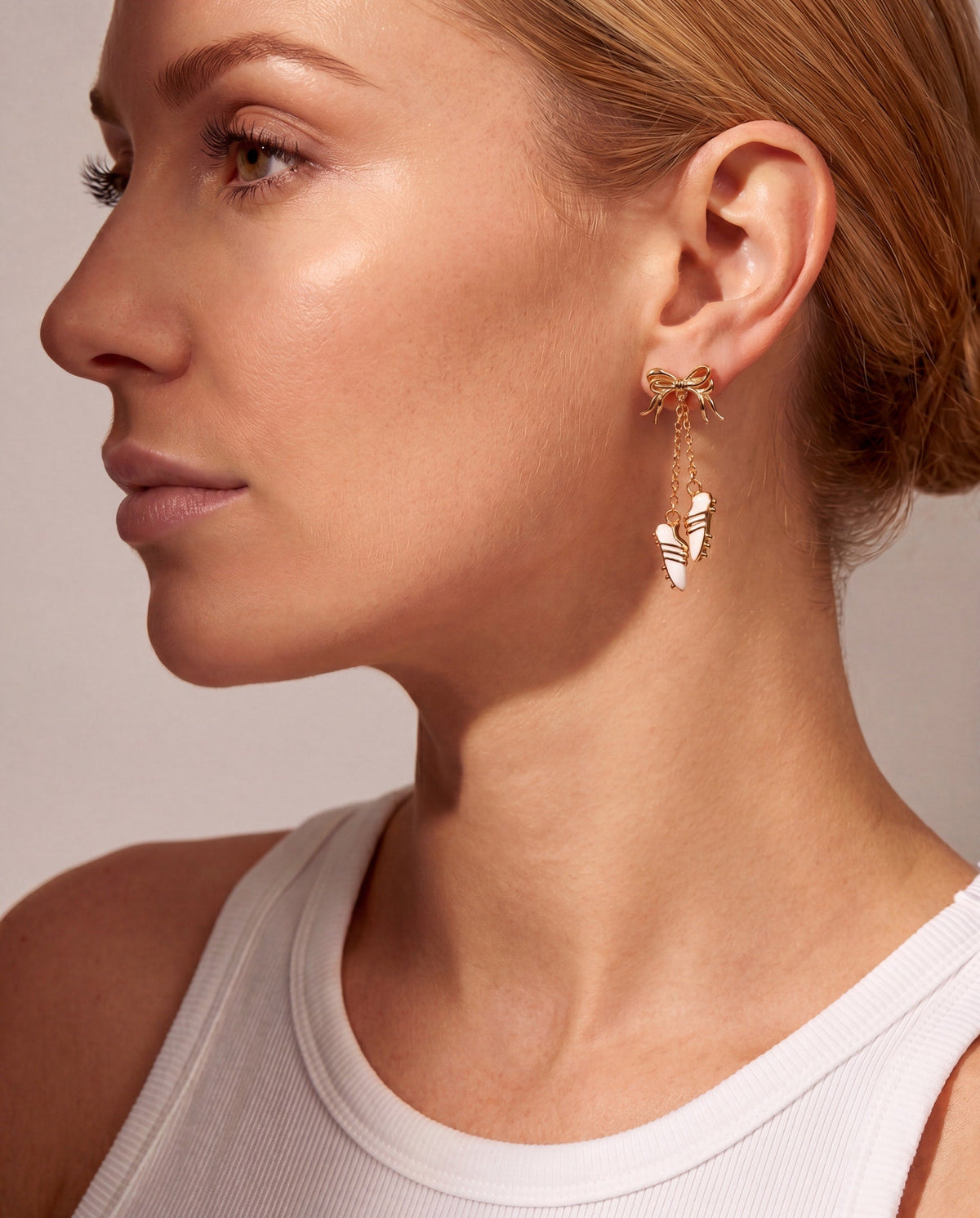 Gold-tone soccer cleat dangle earrings on ear with bow detail and chain tassels