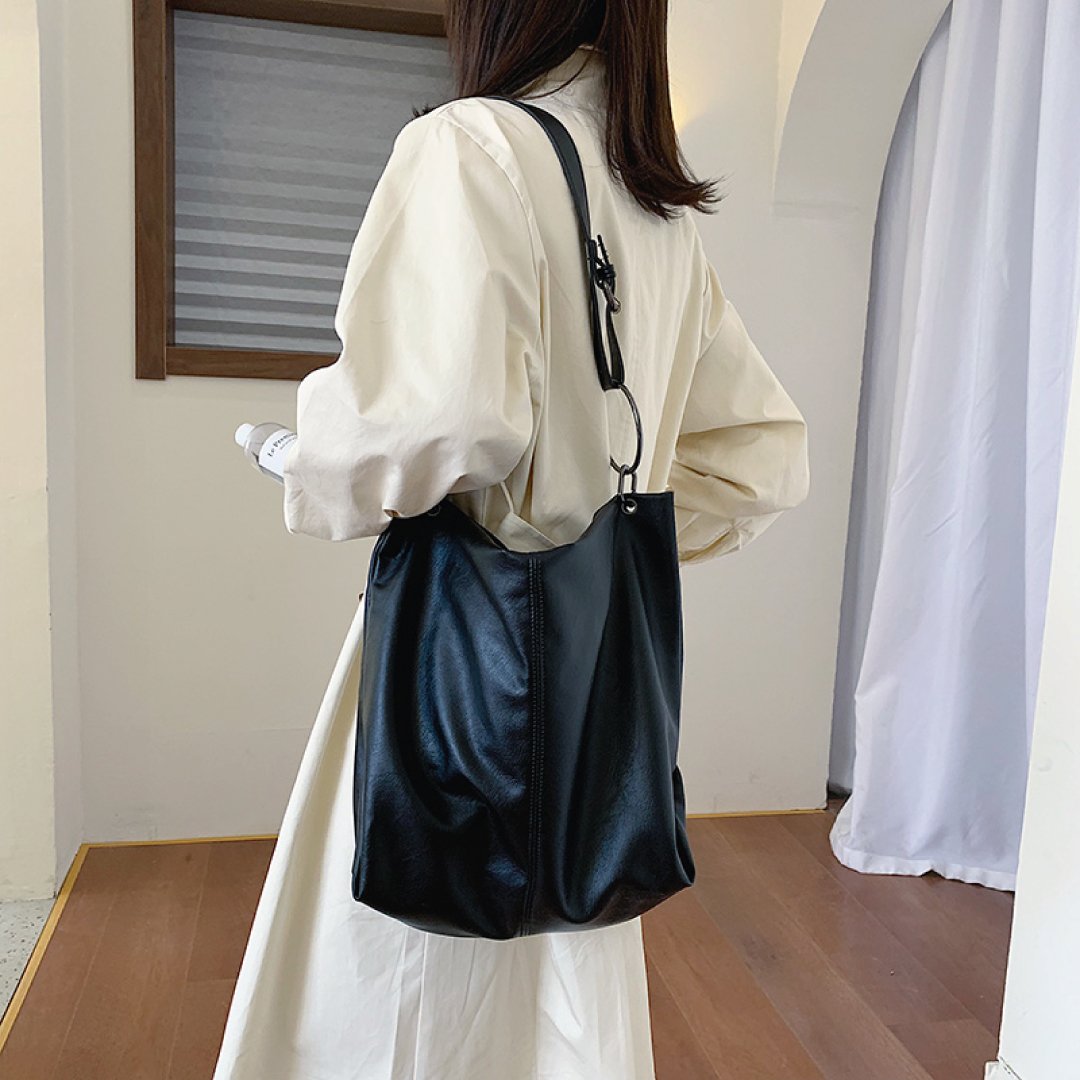 Black shoulder bag with wide strap, ring hardware, and top zipper closure