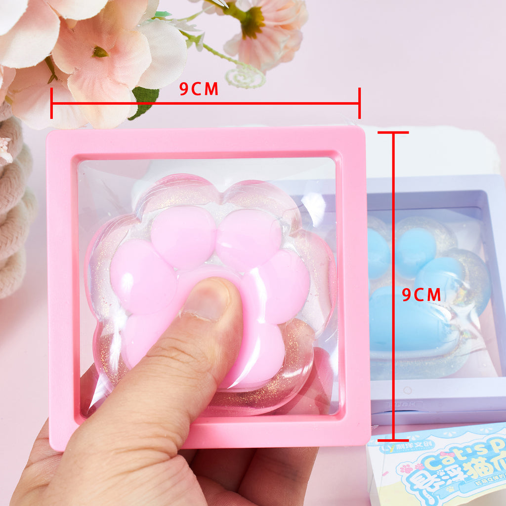 Pink cat-paw squeeze toy in a clear tray, hand pressing; size marking shows 9cm