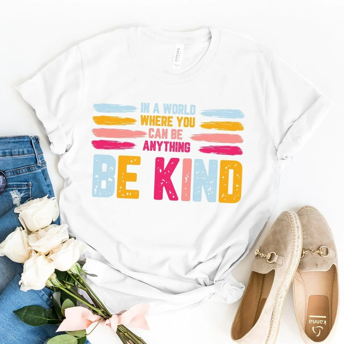 White Be Kind slogan tee with colorful “BE KIND” print and tie-front knot