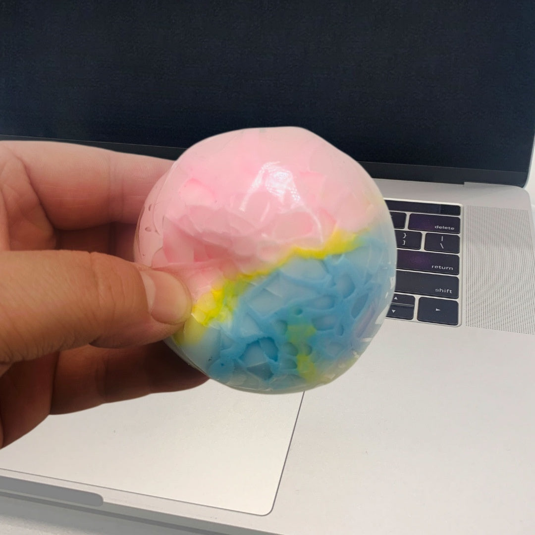 Pastel blue and pink crispy sphere stress-relief squeeze toy, held in hand