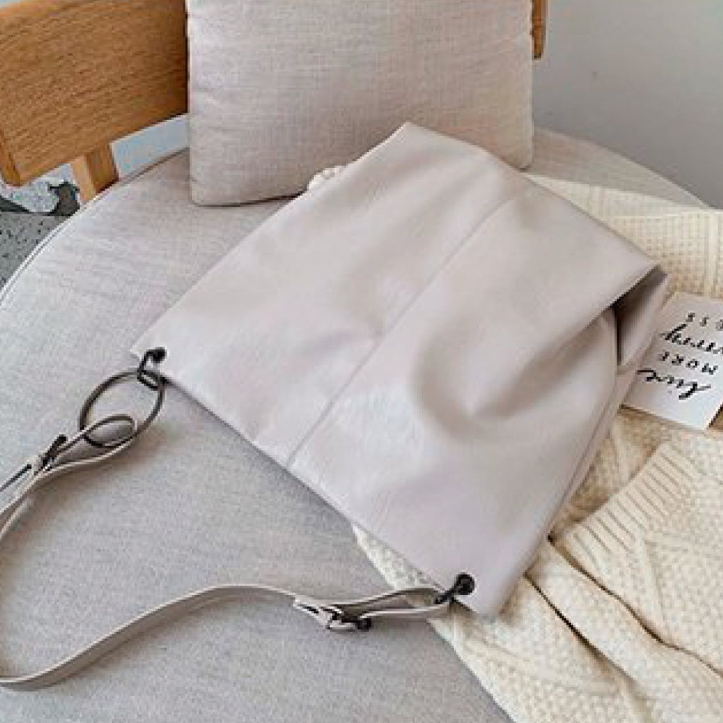 Ivory shoulder bag with long strap and metal ring clasp on sofa