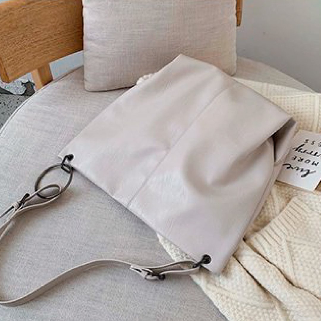Ivory shoulder bag with long strap and metal ring clasp on sofa