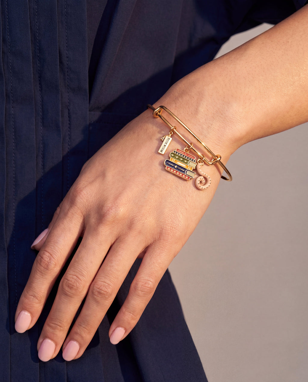 Gold multicharm bangle with book stack charms and pink octopus charm on wrist