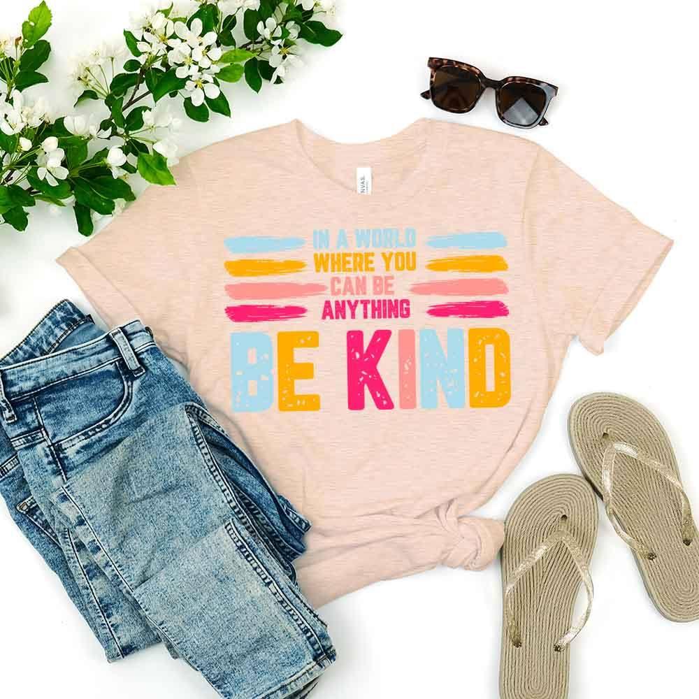 Light pink Be Kind slogan tee with colorful “BE KIND” print and tied front