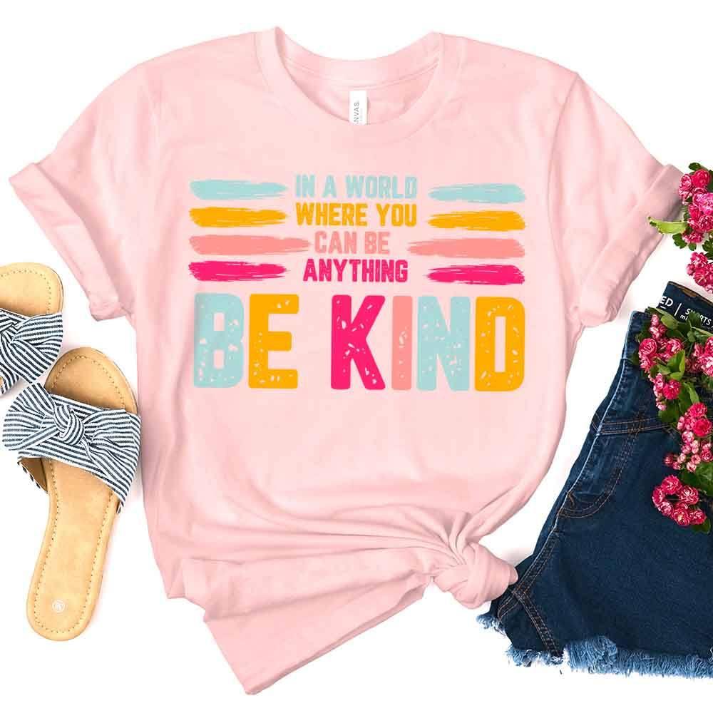 Soft pink Be Kind graphic tee with colorful “BE KIND” print and slogan text