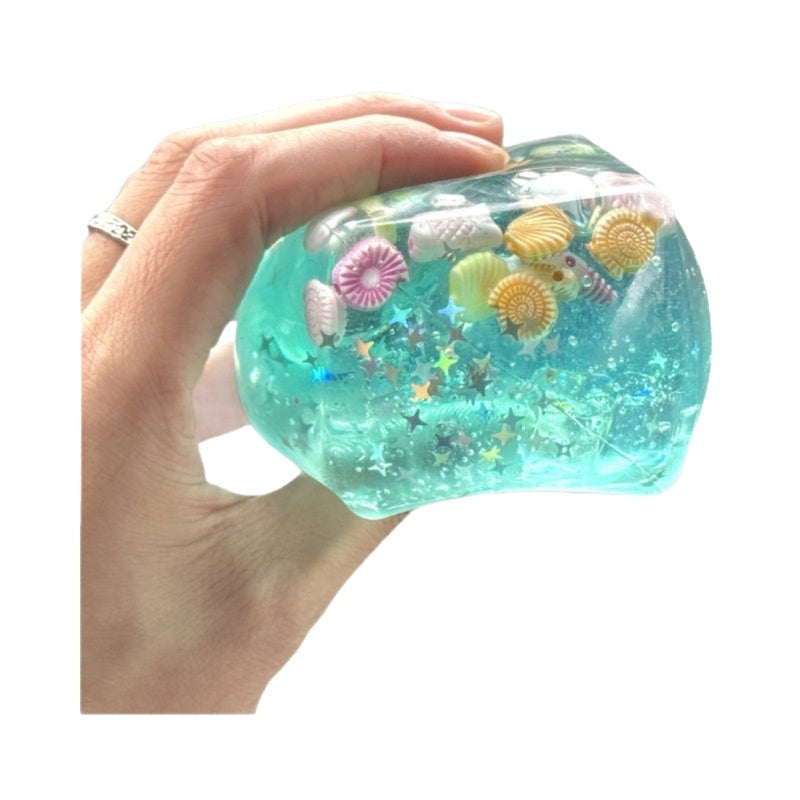 Aqua blue translucent squeeze cube toy with seashell graphics held in hand