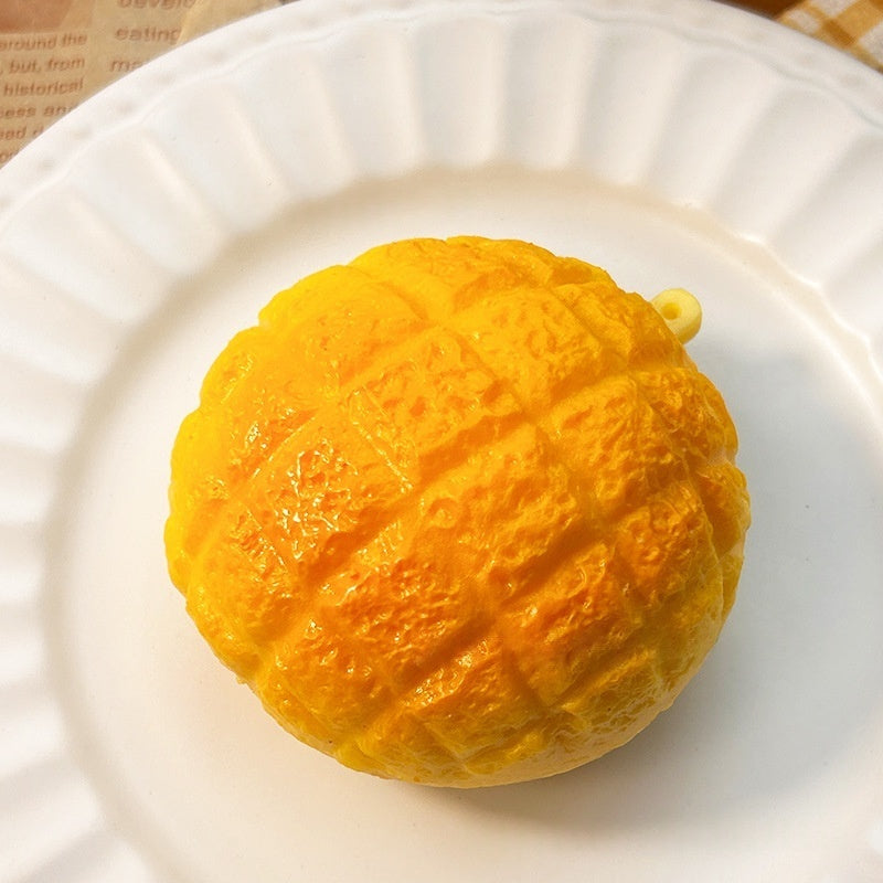 Orange pineapple bun squishy toy on a white plate, textured surface