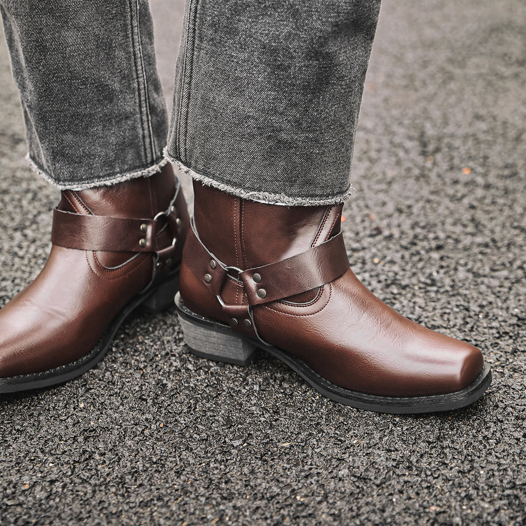 Brown western cowboy boots with square toe, chunky heel, decorative buckle straps.