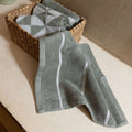 Sage green cotton towel with white stripe and diamond pattern, laid in a basket