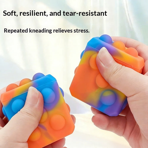 Square silicone bubble stress ball with rainbow bumps, held and squeezed by two hands