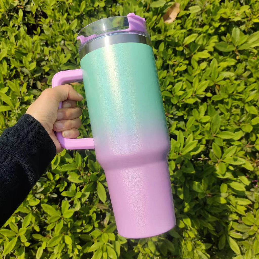 Insulated stainless steel tumbler with mint-to-pink gradient finish, handle, and clear lid
