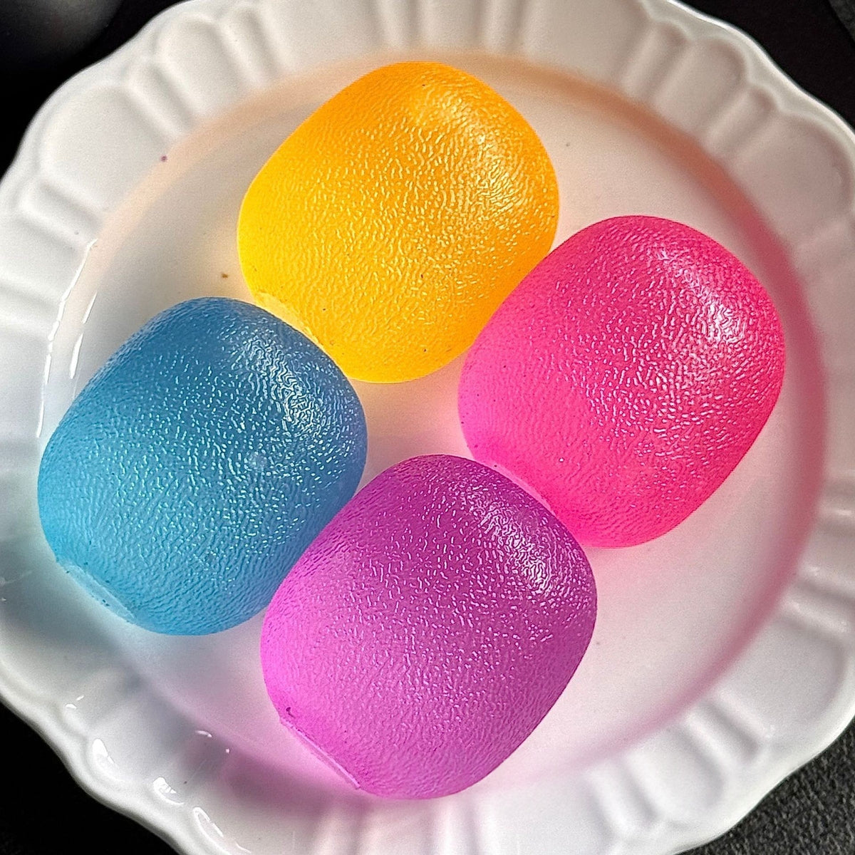 Color-changing squishy squeeze toy balls in blue, yellow, pink, and purple on a plate
