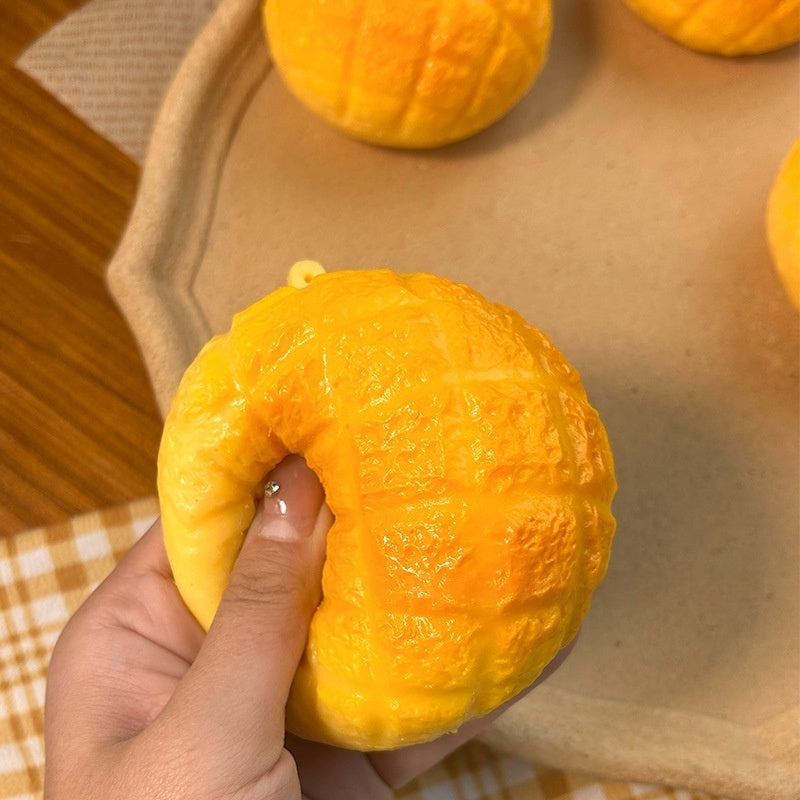 Orange pineapple bun squishy toy with top loop, held in a hand