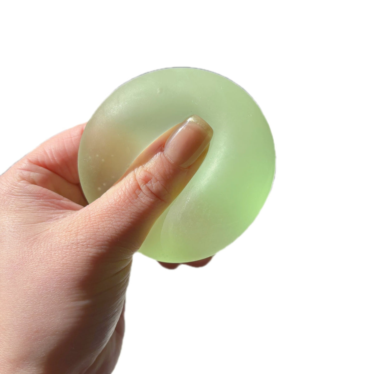 Translucent round squishy candy squeeze toy, light green, held in hand