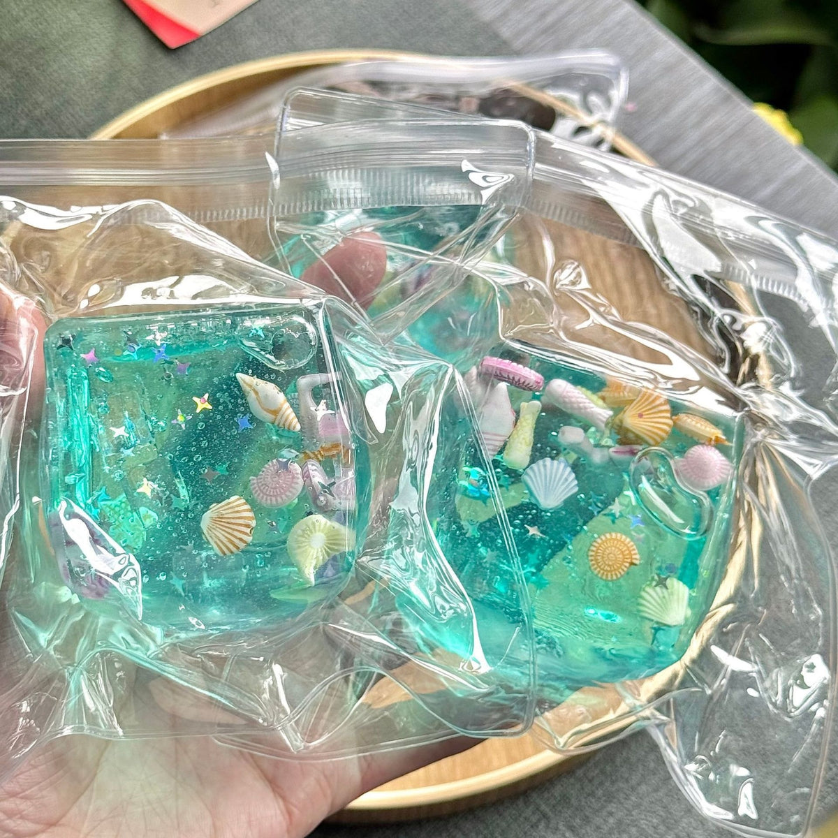 Translucent aqua blue squeeze cube toy inside clear plastic wrapping, ocean-themed icons