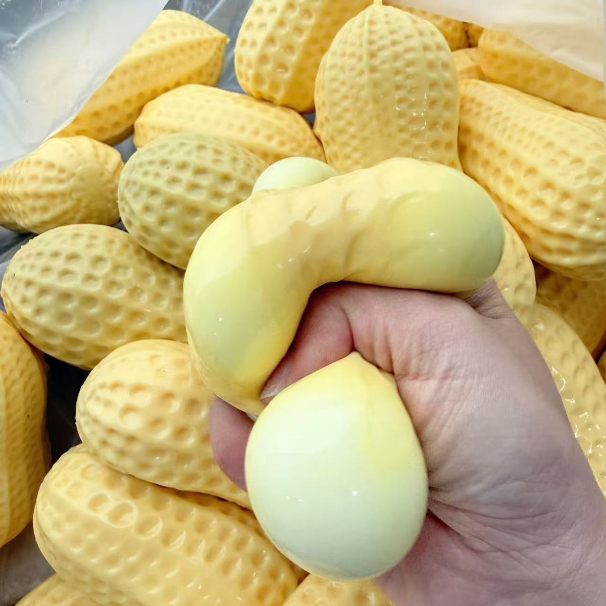 Soft yellow peanut squeeze stress toy being pressed in hand