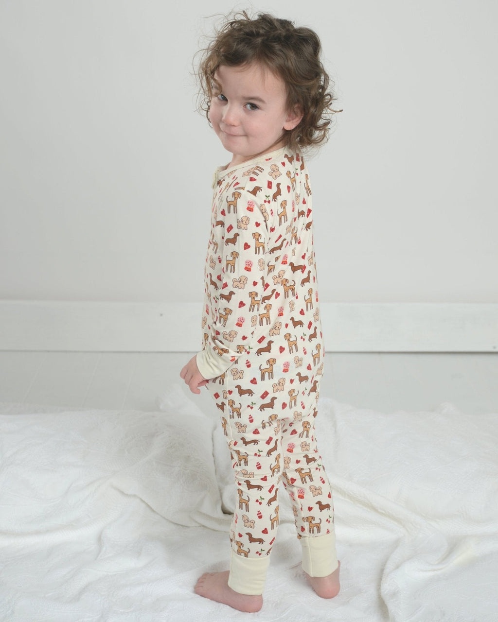 Toddler dog-print pajama romper with front zipper and long sleeves, cream fabric, standing