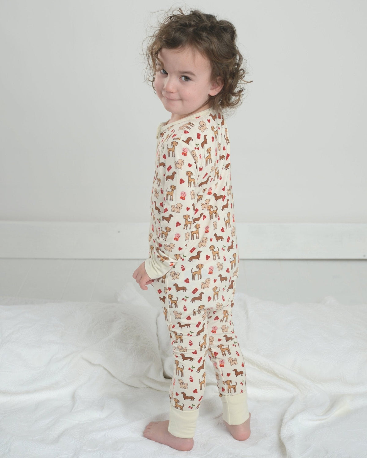Toddler dog-print pajama romper with front zipper and long sleeves, cream fabric, standing