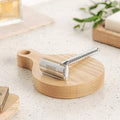 Chrome safety razor with textured grip and stand on round wooden base
